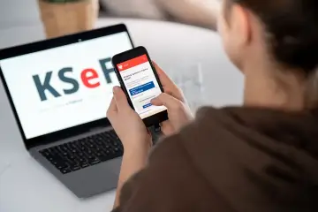 Kobieta korzysta z telefonu z aplikacją KSeF, gdzie widnieje informacja o fakturze ustrukturyzowanej. Laptop obok wyświetla logo KSeF.