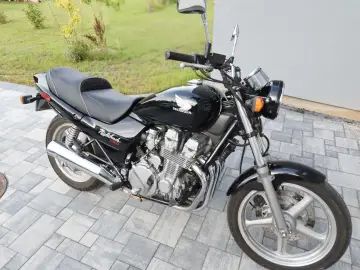 Czarny motocykl Honda CB750 Nighthawk z chromowanymi elementami, zaparkowany na kostce brukowej.