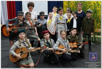 Dzieci w strojach harcerskich grają na gitarach i mandolinie. To może być zapowiedź piosenki o harnasiu.