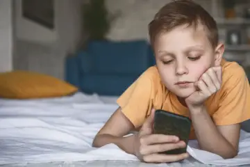 Chłopiec leży na łóżku z telefonem, zastanawiając się, czy dziecko może usunąć Family Link.