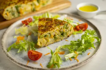 Pyszny omlet z piekarnika z warzywami, podany z sałatką i pomidorkami.