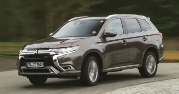 Brązowy Mitsubishi Outlander PHEV jedzie po drodze, zamazane tło sugeruje ruch.