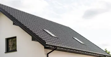 Nowy dach z dachówki w kolorze RAL 9011, z oknem dachowym i białym tynkiem.