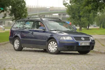 Ciemnoniebieski Volkswagen Passat kombi, model b5, stoi na brukowanym placu.