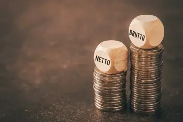 Drewniane kostki z napisami "BRUTTO" i "NETTO" na stosach monet. Zastanawiasz się, ile to netto z 31,40 brutto na umowie zlecenie?