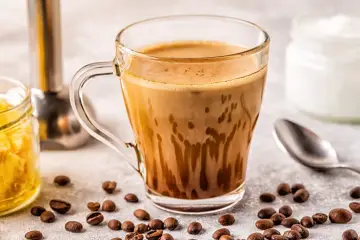 Kawa bullet coffee w szklance, obok ziarna kawy, słoiczek z miodem i łyżeczka.