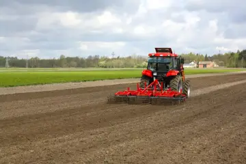 Czerwony traktor z agregatem uprawowym na polu. Przygotowanie gleby pod zasiew, jak wniosek o przedłużenie umowy dzierżawy kowr wzór.