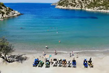 Linia pojazdów terenowych na plaży w Poros, Grecja, czeka na chętnych do zwiedzania. W tle turkusowe morze i skaliste wybrzeże.