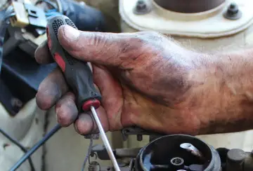 Brudna ręka mechanika przykręca śrubę, kontynuując wymianę linki sprzęgła w samochodzie.