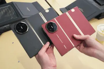 Dwie składane wersje Huawei Mate XT Ultimate w kolorze czarnym i czerwonym, prezentowane przez dłonie.