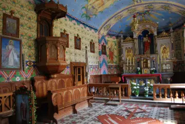 Wnętrze kościoła w Bukowinie Tatrzańskiej. Drewniana ambona, ławy i ołtarz zdobią kolorowe malowidła.