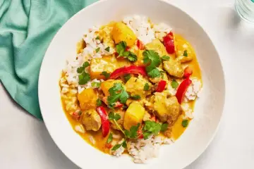 Aromatyczny kurczak curry z ryżem, papryką i kolendrą, podany w białej misce.