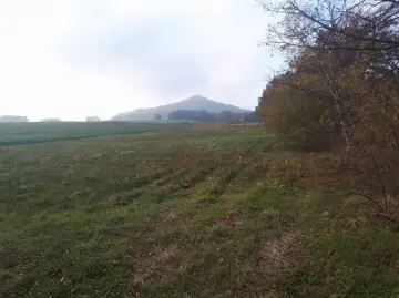 Mglisty poranek nad polami, w oddali majaczy ostrzyca proboszczowicka. Jesienne drzewa szumią przy ścieżce.