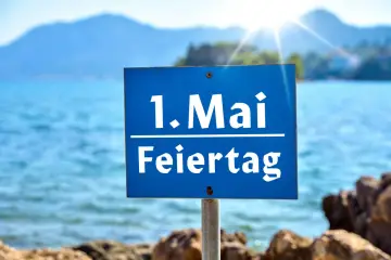 Schild am Strand: "1. Mai Feiertag". Die Sonne scheint über dem Meer, ideal für Veranstaltungen am 1. Mai.