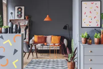 Nowoczesny salon z sofą, fotelami i stolikami. Dominują zimne kolory ścian i mebli, przełamane ciepłymi akcentami poduszek i dekoracji.