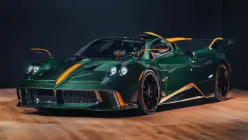 Pagani Huayra w kolorze głębokiej zieleni z pomarańczowymi akcentami, prezentuje swoje karbonowe nadwozie na drewnianej podłodze.