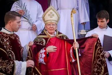 Biskup w czerwonej szacie i mitrze, trzymający pastorał, otoczony przez ministrantów.