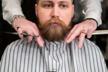 Mistrz precyzyjnie zajmuje się modelowaniem brody klienta, używając nożyczek i grzebienia.