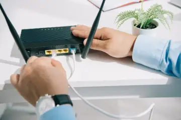 Mężczyzna podłącza kabel do czarnego rutera z dwiema antenkami.