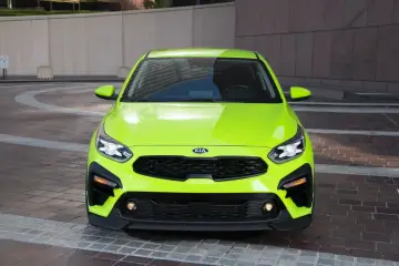 Jaskrawozielony Kia Forte z czarnym grillem i detalami, zaparkowany na brukowanym placu przed budynkiem.