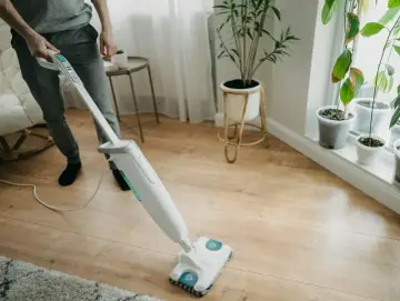 Osoba czyści panele podłogowe mopem parowym. Czy mop parowy niszczy panele? Zobacz, jak skutecznie i bezpiecznie pozbyć się zabrudzeń.