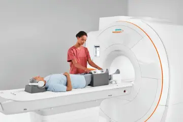 Pacjent leży na łóżku rezonansu magnetycznego, a technik przygotowuje jego nogi do badania. To właśnie mri co to za badanie, które pozwala zajrzeć do wnętrza ciała.