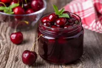 Słoik z konfiturą z wiśni, ozdobiony listkiem mięty. Idealny pomysł, co zrobić z czeresni, gdy jest ich dużo.
