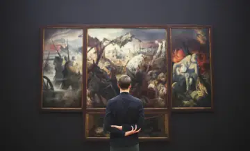 Mężczyzna wpatruje się w tryptyk przedstawiający sceny wojenne, dzieło znanych malarzy.