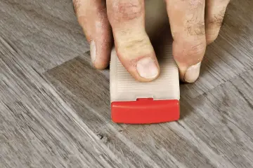 Fingrar använder en kil för att laga laminatgolv.
