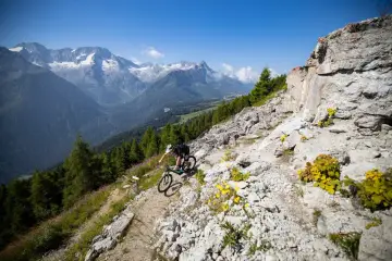 Ciclista in discesa su sentiero roccioso, con montagne innevate sullo sfondo, durante il giro dei forti tonale.
