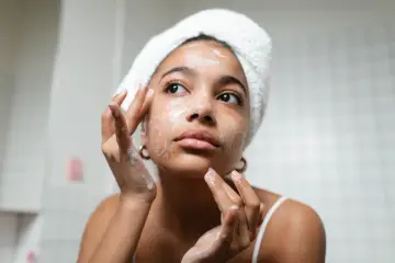 Una joven con toalla en la cabeza se aplica espuma en el rostro, parte esencial de su rutina de skincare.