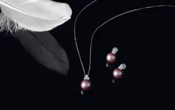 A delicate necklace and earrings featuring pink pearls, symbolizing love and purity. A white feather rests nearby, adding an ethereal touch.
