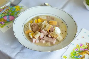 Biały barszcz z kiełbasą, jajkiem i chlebem w talerzu, obok serwetki z zajączkiem.