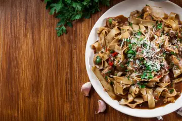 Pyszne danie z makaronem malfadine czy tagliatelle z grzybami i parmezanem, podane na drewnianym blacie.