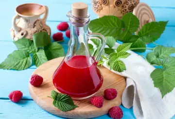 Malinowy ocet balsamiczny do sałatek, deserów, marynat. W butelce z korkiem, otoczony świeżymi malinami i liśćmi.