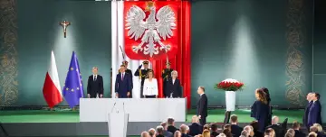 Uroczysta chwila, gdy prezydent wygłasza orędzie. Na scenie flagi Polski i UE, godło, a także osoby w mundurach.