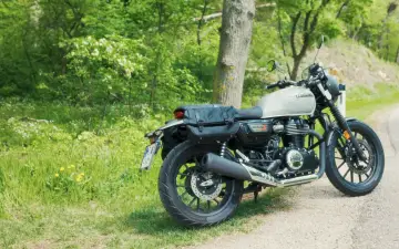 Klasyczny motocykl Honda GB350 z sakwami, zaparkowany na poboczu drogi wśród zieleni i kwitnących krzewów.