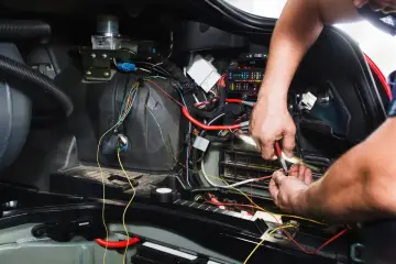 Mechanik naprawia okablowanie w samochodzie. Może to być związane z objawami silniczka krokowego, takimi jak nierówna praca silnika.