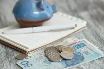 Świnka skarbonka, notatnik i długopis nad polskimi banknotami i monetami. Zastanawiasz się, ile wyniesie waloryzacja kapitału początkowego w 2025?