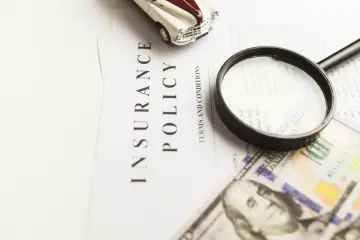 Model samochodu, lupa i pieniądze na dokumencie "Insurance Policy". Sprawdzam, czy podlegam obowiązkowi ubezpieczenia zdrowotnego.