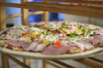 Surowa pizza z szynką, cebulą i kolorową papryką. Wszystkie składniki na pizzę ułożone na cieście, gotowe do pieczenia.