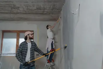 Para malują ściany, tworząc subtelne paski. On z wałkiem w ręku, ona na drabinie.