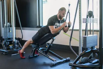 Mężczyzna wykonuje ćwiczenie na triceps, znane jako skull crushers, na ławce skośnej z użyciem wyciągu.