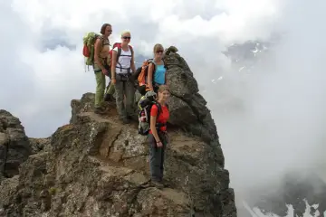 Quattro escursionisti con zaini si fermano sulla cima rocciosa di Cima Sternai, circondati da nuvole e nebbia.