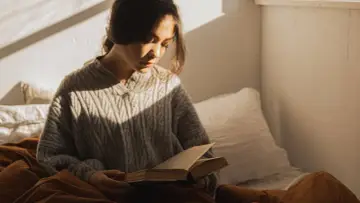 Dziewczyna w swetrze czyta książkę w łóżku, pogrążona w świecie, gdzie logika ustępuje miejsca irracjonalizmowi.