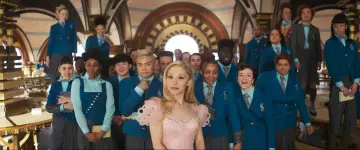 Ariana Grande w różowej sukience wśród uczniów w niebieskich mundurkach. Scena z jednego z jej filmów.