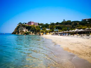Piękne, turkusowe morze na Zakynthos. Plaża z leżakami i parasolami, a na klifie hotel.