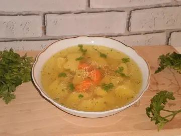 Aromaticzny rosół z ziemniakami i marchewką, ozdobiony natką pietruszki, podany w białej miseczce na drewnianej desce.