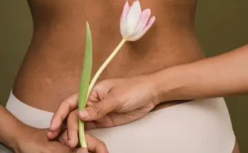 Delikatne rozstępy na plecach, ukryte za tulipanem. Ciało w beżowej bieliźnie.