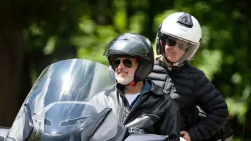 Uśmiechnięty mężczyzna w kasku i okularach przeciwsłonecznych, z pasażerką na motocyklu. Idealny wybór, jaki motocykl dla 50-latka?